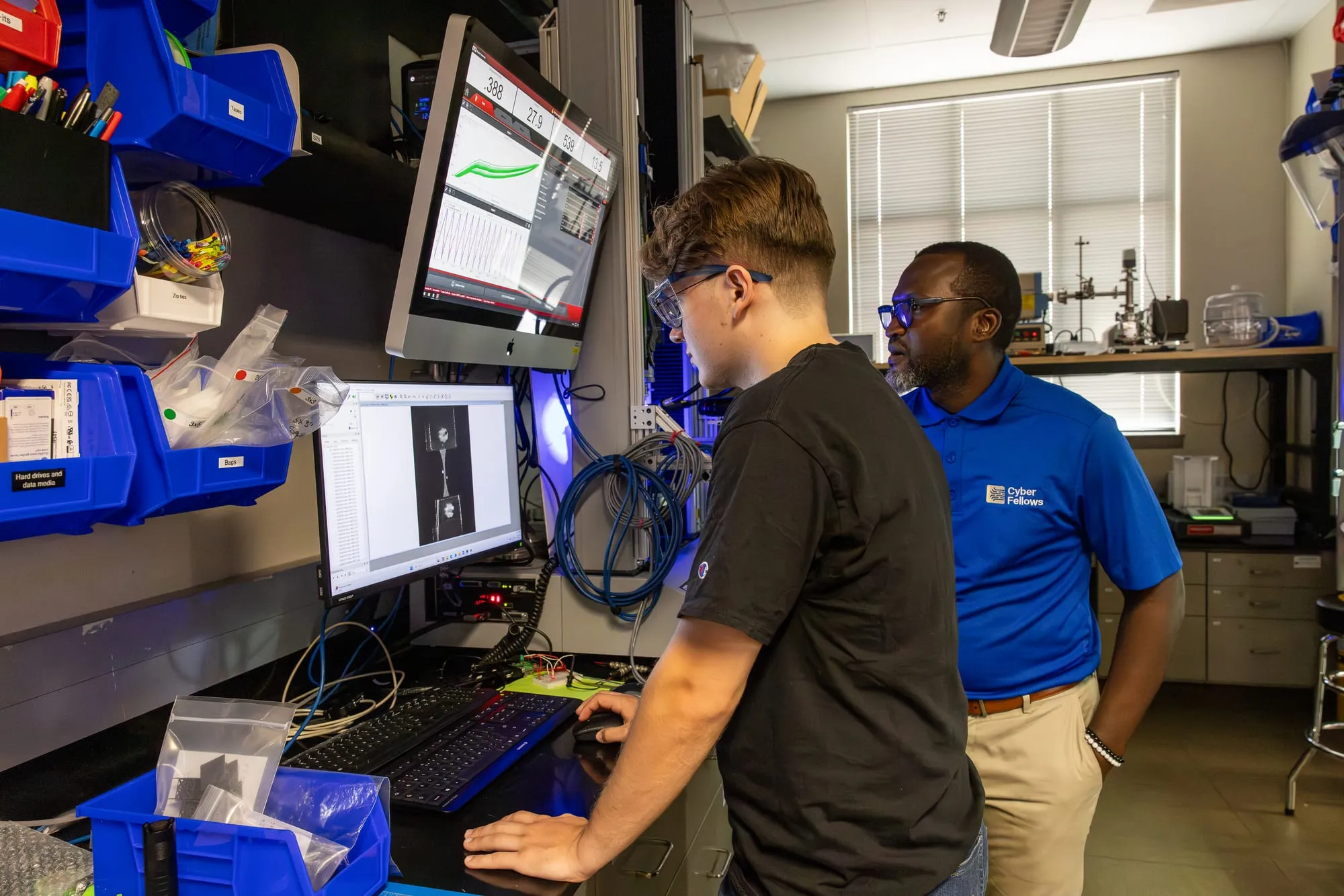 Two researchers at the Gimli control station, with live load–displacement data and a DIC image of the specimen on the monitors.
