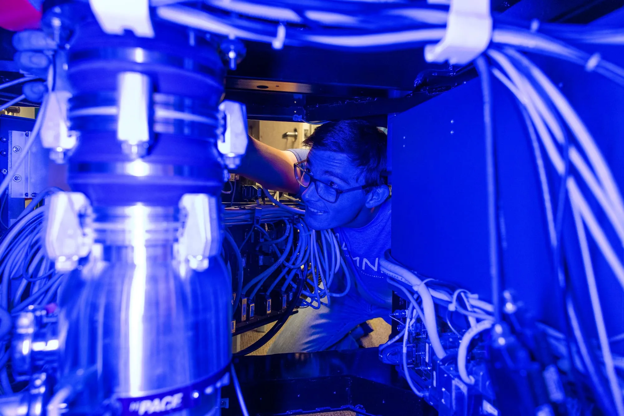 AMDG member replaces the vacuum gauge in the Helios dual-beam scanning electron microscope, lit by blue light.