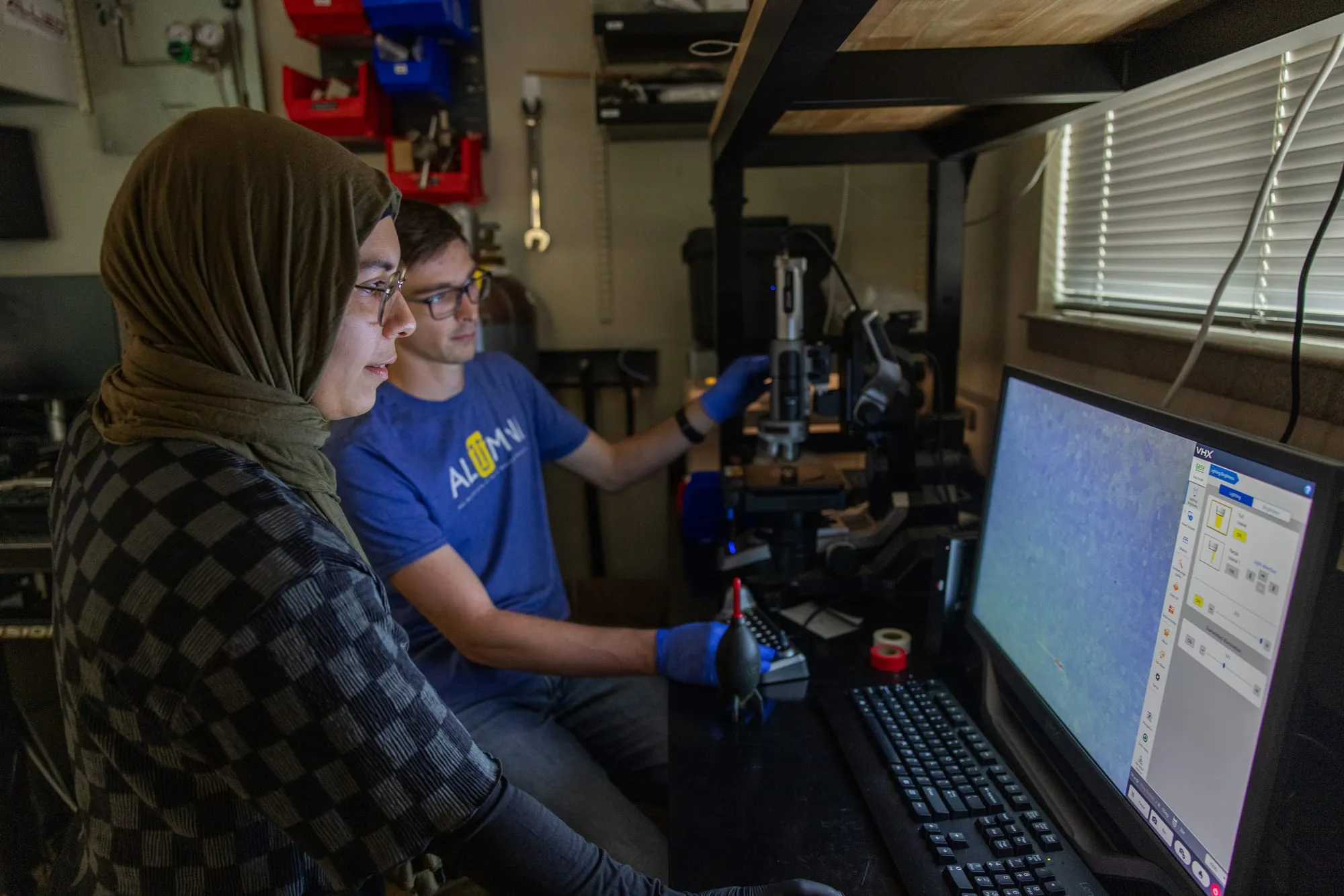 Two AMDG members examine a micrograph on the Keyence digital microscope's display.