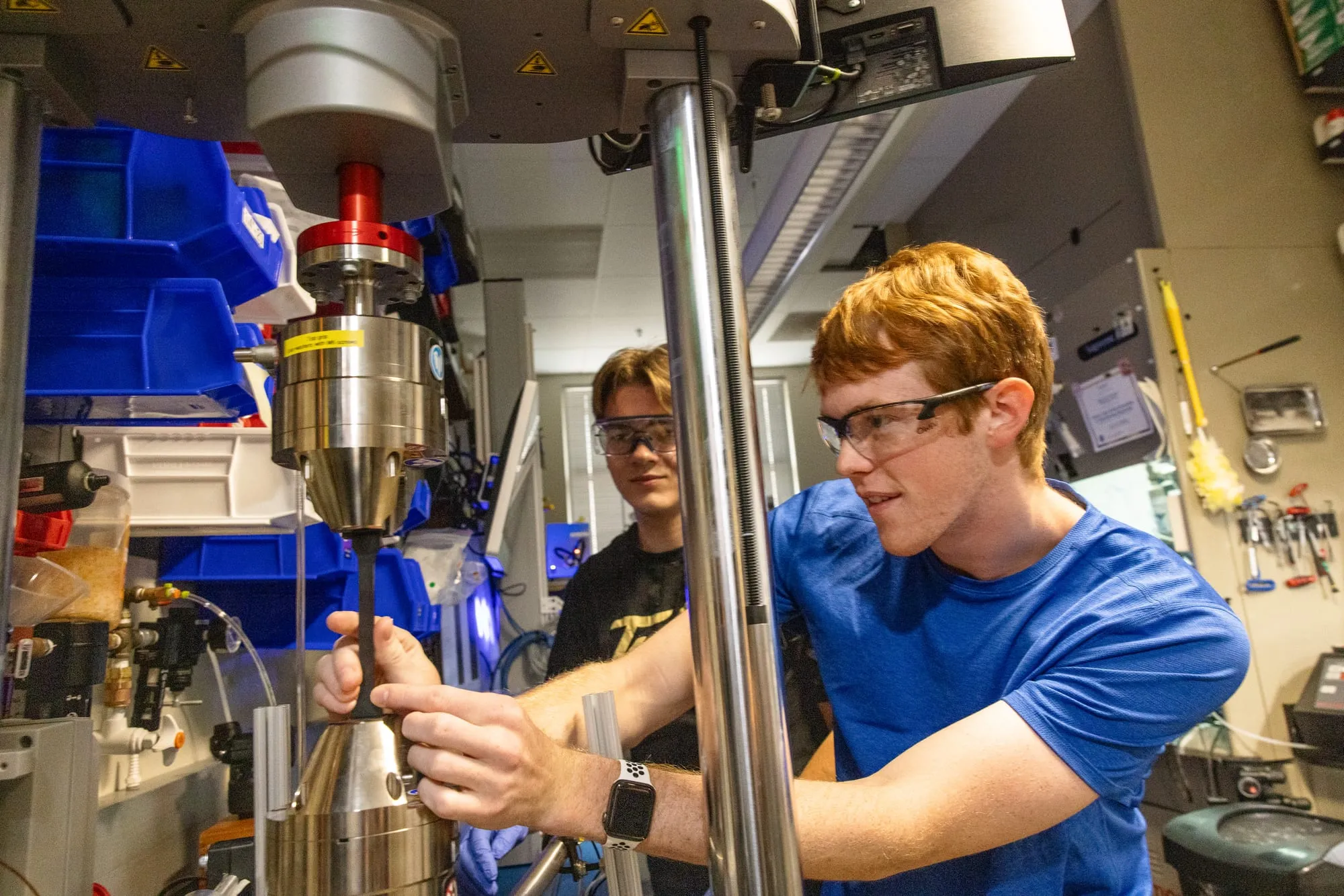 A student threads a specimen into the grips of the Instron E3000 while a second student looks on.
