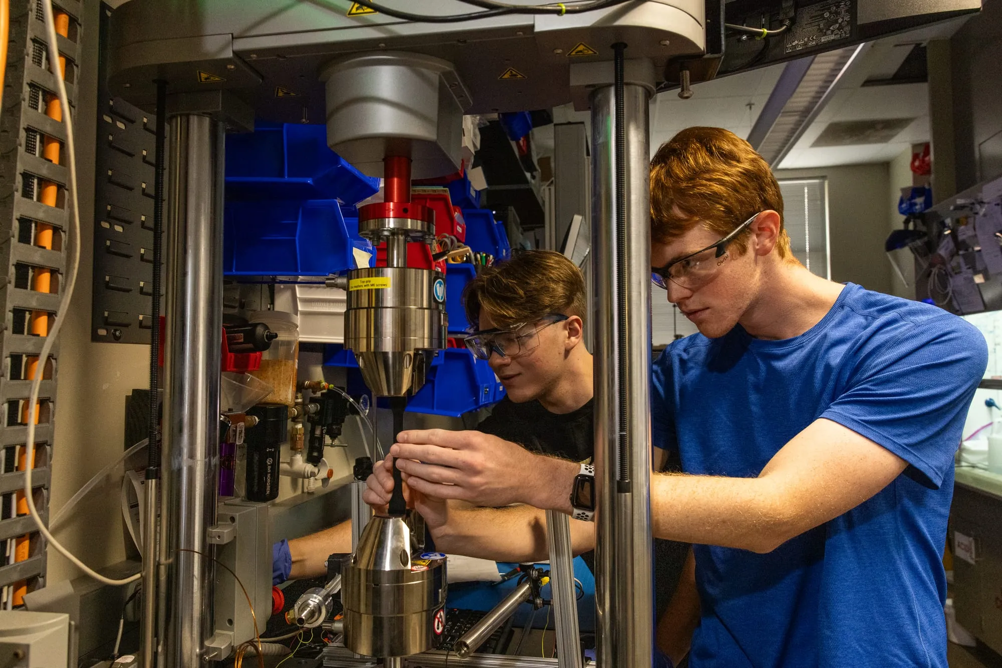 Two AMDG members in safety glasses mount a specimen into the grips of a load frame.