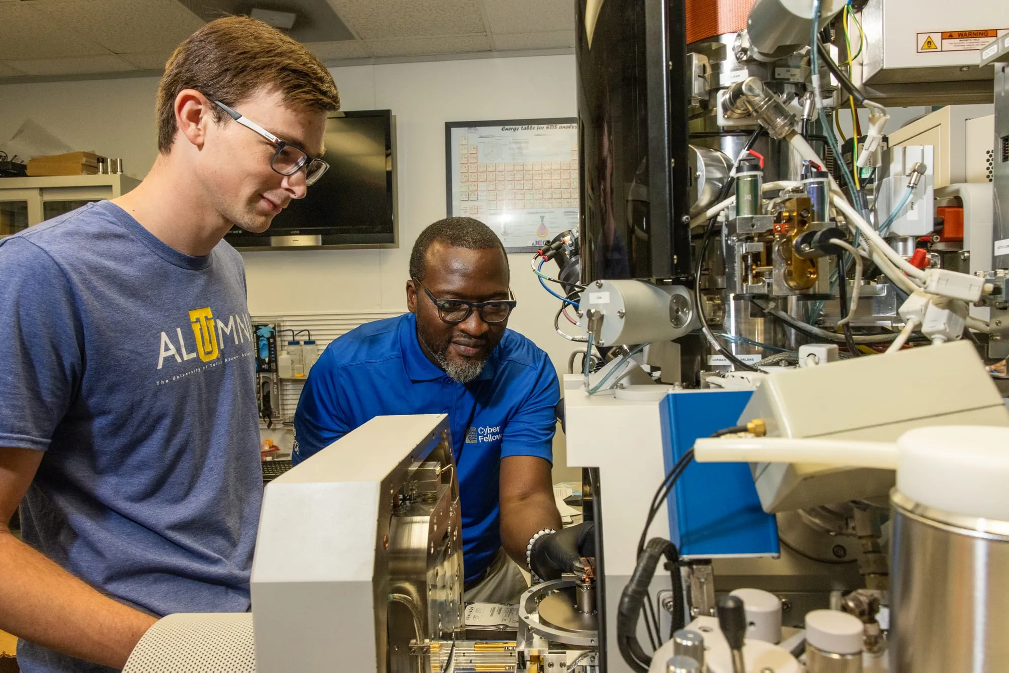 Two AMDG members load a sample into the Helios dual-beam scanning electron microscope in the materials lab.
